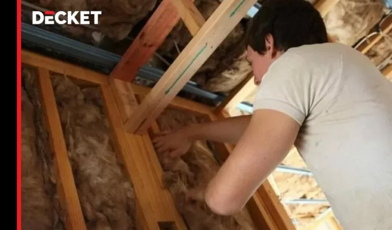 Pracownik montujący izolację z wełny mineralnej między drewnianymi belkami konstrukcji dachu.