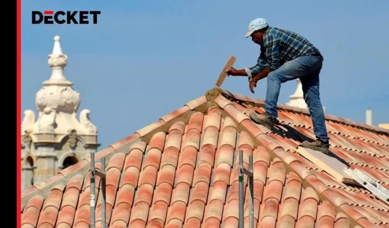 Dekarz pracujący na dachu z dachówek, używający narzędzi do naprawy i uszczelniania kalenicy.