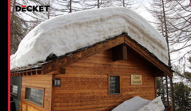 Drewniany domek z dachem obciążonym grubą warstwą śniegu, przykład wpływu stref obciążenia śniegiem na konstrukcję dachu.